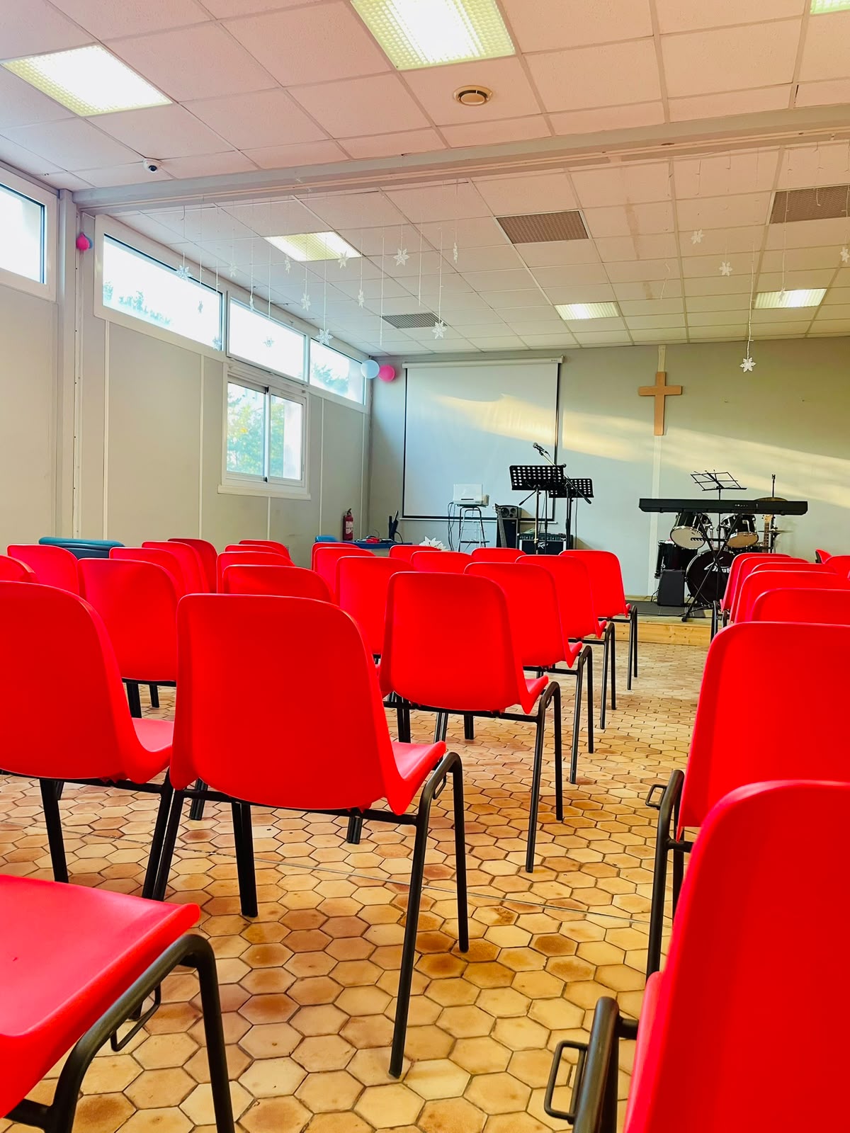 Interior of the Emmanuel Evangelical Church hall with red chairs, projector screen, and worship instruments